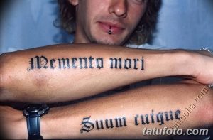 Фото тату двух готических надписей 'Memento Mori' и 'Duum Tuique' на предплечьях. Черный рисунок татуировки выглядит мощно и символично.