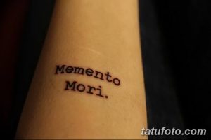 Фото тату надписи 'Memento Mori' простым шрифтом на руке. Черный рисунок татуировки выглядит лаконично и стильно.