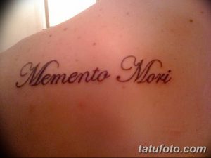 Фото тату надписи 'Memento Mori' изящным шрифтом на плече. Черный рисунок татуировки выглядит элегантно и сдержанно.