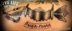 Фото тату на руке с изображением рыбы, пронзенной пилами. Надпись 'Рыба-пила' выполнена красным цветом.