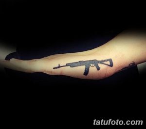 Фото тату автомата на предплечье. Черный силуэт оружия, выполненный в минималистичном стиле. Идеально для тех, кто предпочитает лаконичные рисунки.