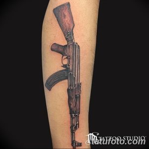 Черно-серая татуировка автомата Калашникова на ноге. Детализированный рисунок с проработкой текстур и теней.
