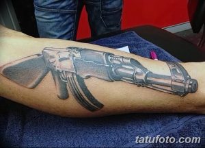 Реалистичная черно-серая татуировка автомата Калашникова на руке. Детализированный рисунок с проработкой текстур и теней.