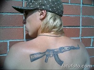 Фото тату АК-47 на мужской лопатке. Реалистичный рисунок автомата Калашникова в серо-черных тонах. Подробный эскиз татуировки для мужчин.