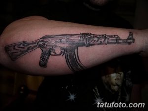 Фото тату реалистичного автомата Калашникова на руке. Детализированный рисунок татуировки, выполненный в серо-черной гамме, имитация металла и дерева.