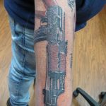 Фото тату автомата Калашникова в стиле графика на руке. Черно-белый рисунок татуировки, выполненный тонкими линиями, с добавлением штриховки и теней.