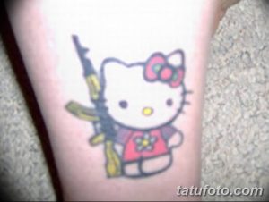 Фото забавной татуировки Hello Kitty, держащей автомат Калашникова, выполненной в ярком мультяшном стиле.