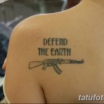 Фото татуировки автомата Калашникова с надписью 'Defend the Earth', выполненной черным цветом на спине.