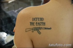 Фото татуировки автомата Калашникова с надписью 'Defend the Earth', выполненной черным цветом на спине.