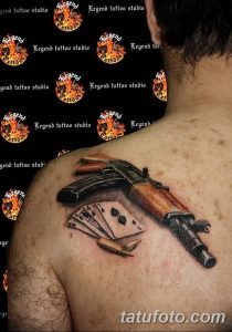 Фото татуировки на груди с изображением пистолета, карт и револьвера, выполненной в реалистичном стиле.