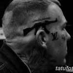 Фото татуировки на голове, изображающей автомат Калашникова и надпись 'LYRICAL ASSAULT'. Черно-белый рисунок.