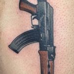 Фото реалистичной татуировки автомата Калашникова на руке. Детализированный рисунок оружия с использованием коричневых и серых оттенков.