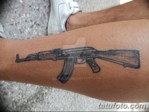 Фото тату на икре: реалистичное изображение автомата Калашникова, выполненное в черно-коричневых тонах. Детализированный рисунок татуировки.