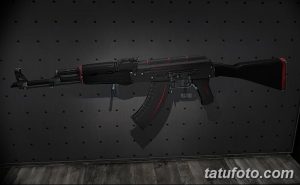 Фото тату стилизованного автомата Калашникова на темном фоне. Рисунок оружия с красными элементами и текстурой карбона.