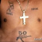 Фото тату на груди 50 Cent с изображением креста, автомата и надписей. Смешение религиозных и уличных символов.