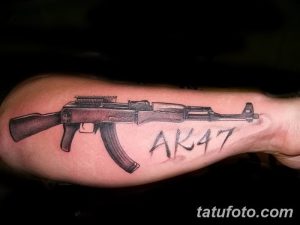 Фото татуировки на предплечье с изображением винтовки AK47 и надписью 'AK47'. Черно-серый рисунок с реалистичными деталями.