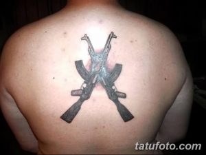 Фото татуировки на спине с изображением двух скрещенных винтовок. Черно-серый рисунок с четкими линиями и контрастным фоном.