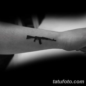 Фото минималистичной татуировки винтовки, выполненной черными линиями на запястье. Простой и лаконичный дизайн.