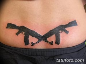Фото тату с изображением двух черных скрещенных винтовок на животе. Четкие линии и контрастный рисунок делают татуировку заметной и выразительной.
