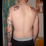 Фото тату на спине мужчины с изображением черных символов Уджат и Анкх, выполненных в минималистичном стиле. Эскиз татуировки подчеркивает духовность и защиту.