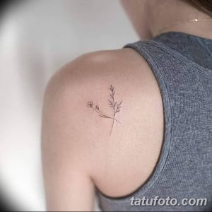 Фотография изящной татуировки с изображением тонкой веточки с маленькими цветами, расположенной на плече. Черно-белое изображение, выполненное в технике лайнуорк.