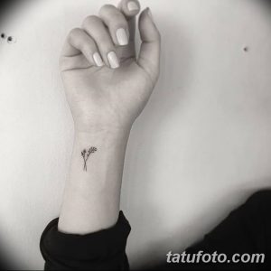 Фото тату: крошечная черная веточка с листьями на женском запястье. Минималистичный рисунок татуировки, выполненный тонкими линиями.