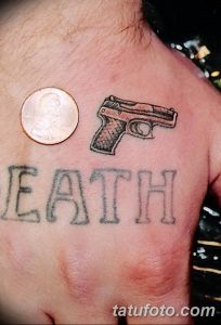 Фото тату: Черно-серая татуировка с изображением пистолета и надписи 'Death' на груди. Провокационный и мрачный рисунок татуировки.