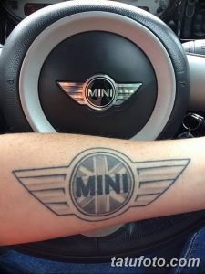 Фото тату: Черно-серая татуировка с изображением логотипа автомобиля MINI на предплечье. Стильный и лаконичный рисунок татуировки.