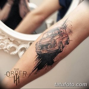 Фото тату реалистичного изображения старинного автомобиля на предплечье, выполненного в черно-серых тонах с добавлением брызг краски.