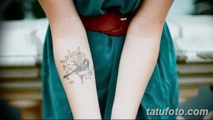 Фото тату птички на ветке с листьями на предплечье. Черно-белый рисунок, выполненный в реалистичном стиле. Изящная и трогательная татуировка.