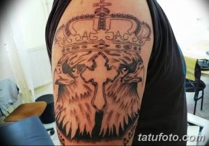 Фото тату креста, увенчанного короной, и двух голов воронов. Чёрно-серые тона, готический стиль, сложный рисунок.