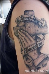 Фото тату креста, обхваченного молящимися руками, с надписью 'In Loving Memory Grandpa'. Черно-белая татуировка на плече, символизирующая скорбь и любовь.