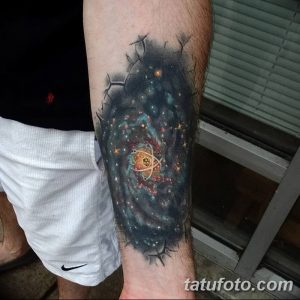 Детализированная татуировка, изображающая атом, окруженный галактикой и звездным небом на руке. Яркий и захватывающий рисунок тату.