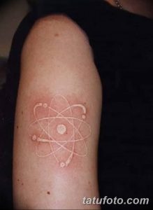 Фото белой татуировки атома на предплечье. Необычный и стильный рисунок, который выглядит как шрам или светящаяся линия.
