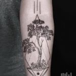 Фото тату: черно-белый рисунок дерева, заключенного в геометрическую фигуру на предплечье. Современный и стильный дизайн.