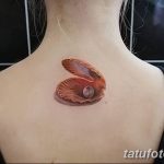 Фото тату: небольшая раковина с жемчужиной на спине девушки. Детализированный рисунок татуировки в реалистичном стиле.