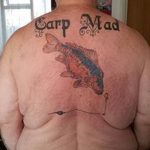 Фото тату карпа кои и надписи "Carp Mad" на спине. Яркие цвета, юмористический стиль. Эскиз татуировки для любителей рыбалки.