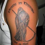 Фото тату Жнеца на плече с надписью 'Death is certain, life is not'. Черно-белый рисунок татуировки в стиле графика.