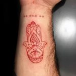 Фото тату Хамса на запястье. Небольшой рисунок татуировки в красных тонах, выполненный в минималистичном стиле.