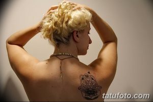 Фото тату Хамса на спине, выполненная в технике blackwork с добавлением небольшого цветка. Изящный рисунок с тонкими линиями и детальной проработкой.