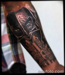 Фото тату: спартанский шлем, выполненный в технике blackwork на предплечье. Множество точек и линий создают эффект тени и объема.