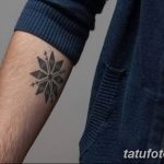 Фото тату: маленькая черная снежинка на предплечье, выполненная в минималистичном стиле. Изящный рисунок татуировки для девушек и парней.
