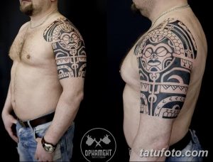 Фото тату: мужское плечо, украшенное сложной татуировкой в полинезийском стиле. Рисунок выполнен в черном цвете и имеет геометрическую форму.