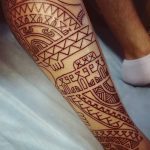 Фото тату: коричневая трайбл татуировка, покрывающая голень. Детализированный рисунок татуировки с геометрическими элементами.