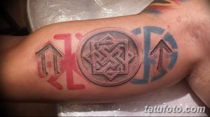 Фото тату на плече, сочетающее славянские символы и кельтский узор. Выполнено в цветном стиле с использованием красного, синего и серого цветов.