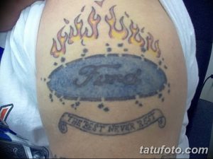 Фото тату: логотип Ford в овальной рамке, окруженный языками пламени, с надписью "The Best Never Rest" на плече.