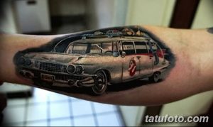 Фото тату: реалистичный черно-серый рисунок автомобиля Ecto-1 из фильма "Охотники за привидениями" на руке мужчины.