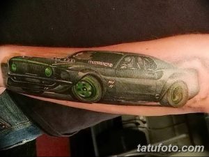 Фото тату на предплечье с изображением автомобиля Ford Mustang в ярких цветах, с зелеными фарами. Детализированный рисунок с эффектом свечения.