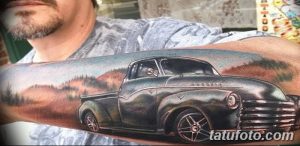 Фотография татуировки на руке с изображением старинного пикапа на фоне горного пейзажа. Детализированный рисунок татуировки.