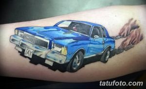 Фотография татуировки на руке с изображением синего автомобиля, оставляющего за собой огненный след. Детализированный рисунок татуировки.